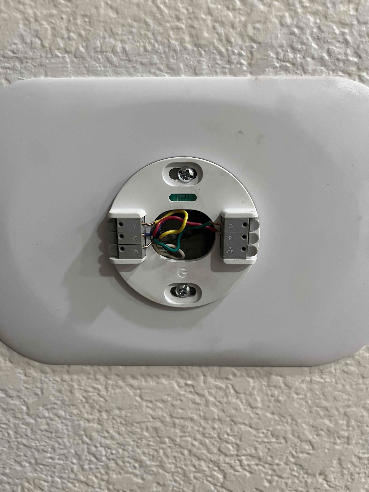 Thermostat mounting base on wall shows connected control wires on labeled terminals Y, W, G, R, C.