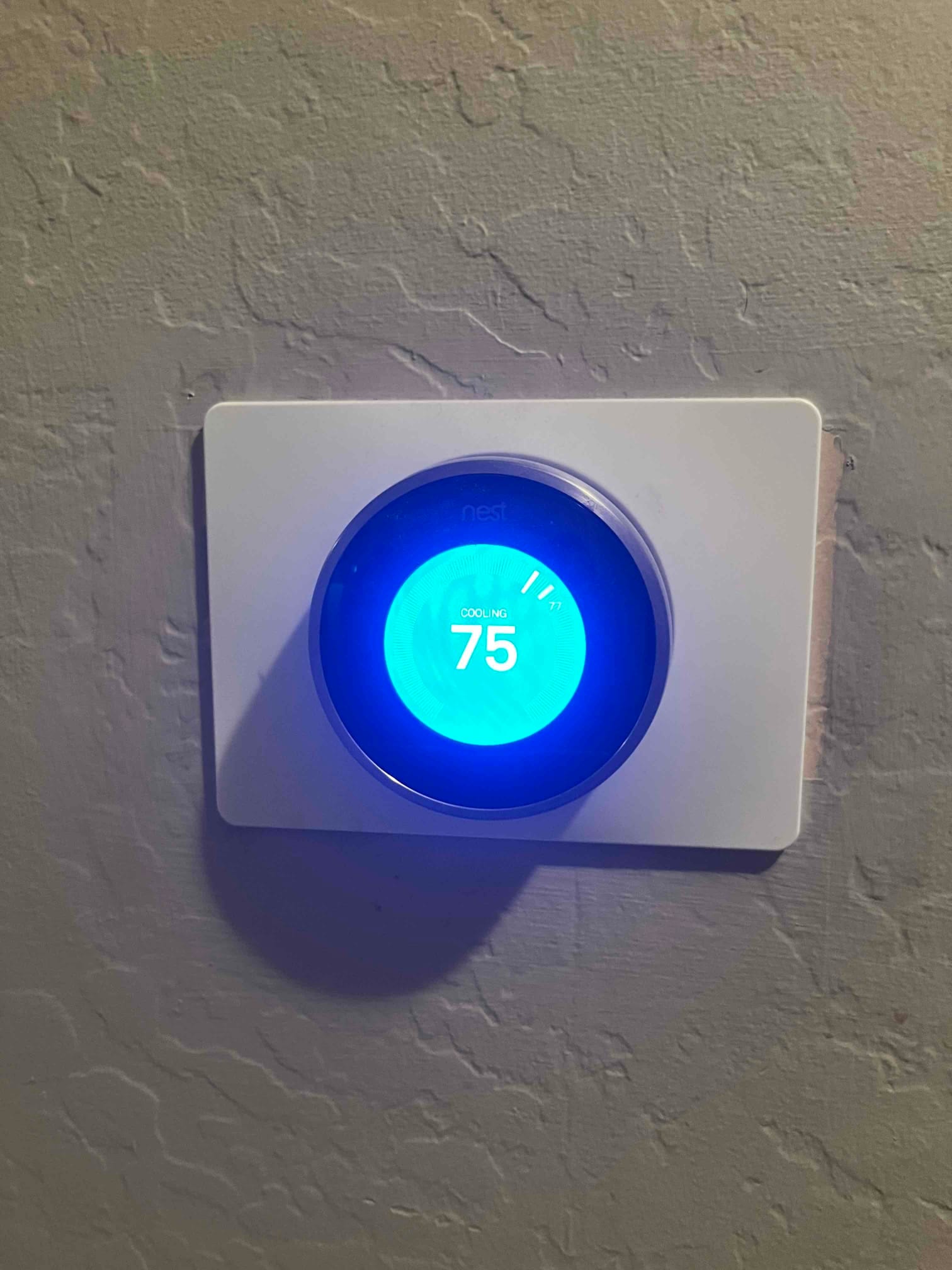 Wall-mounted smart thermostat displays cooling mode with the set temperature at 75 degrees and a blue backlight.