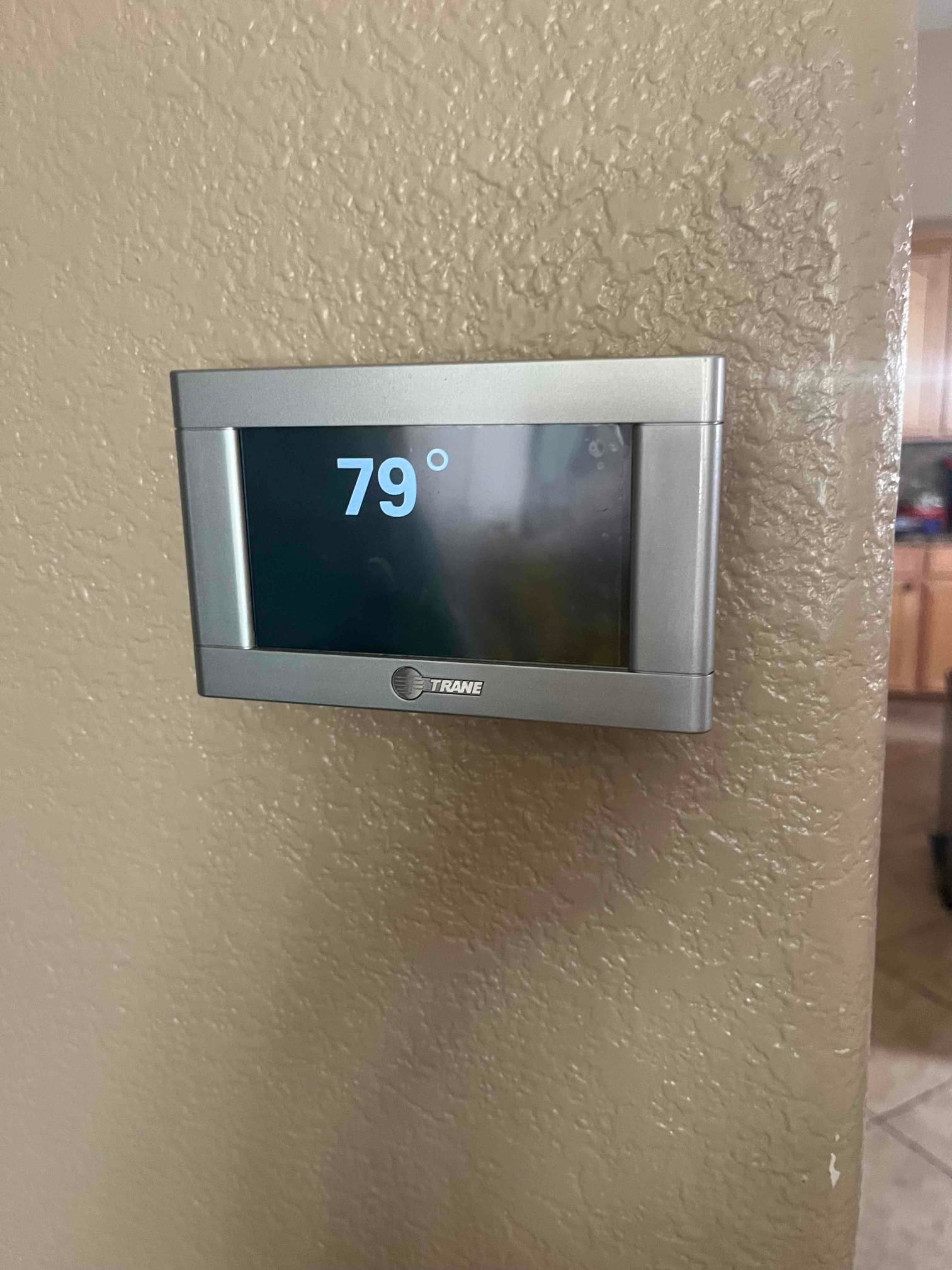 Wall-mounted thermostat displays 79 degrees on its screen inside the home hallway.